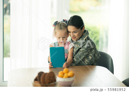 Daughter sitting near mom in military uniform and watching cartoon Daughter sitting near mom in military uniform and watching cartoon 55981952