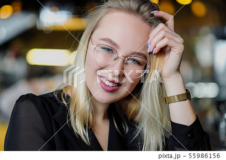 A young beautiful blond woman with glasses sits at the bar in a yellow interior. Drinks alcoholic 55986156