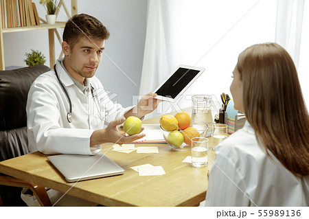 Smiling nutritionist showing a healthy diet plan to patient 55989136