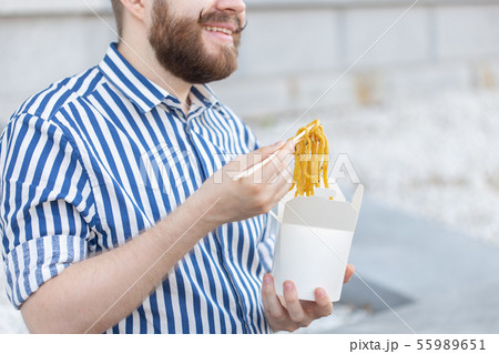 An unidentified young male hipster with a mustache and beard is eating chinese noodles with wooden An unidentified young male hipster with a mustache and beard is eating chinese noodles with wooden 55989651