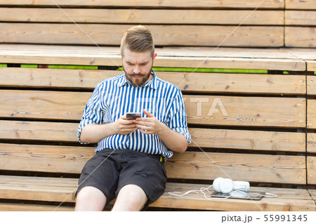 Pensive serious young male hipster student with a mustache and beard writing sms message to his 55991345
