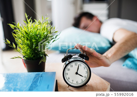 Young tired man hitting alarm clock in bed at home, waking up in morning. Young tired man hitting alarm clock in bed at home, waking up in morning. 55992016