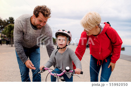 Young family and small daughter with bicycle outdoors on beach. Young family and small daughter with bicycle outdoors on beach. 55992050