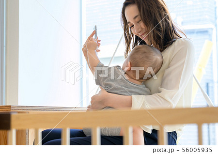 子供を抱きながらスマホを触る女性 子供を抱きながらスマホを触る女性 56005935