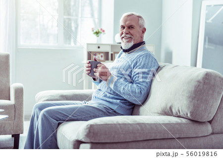 Beaming retired man wearing jeans and blue sweater drinking some tea Beaming retired man wearing jeans and blue sweater drinking some tea 56019816