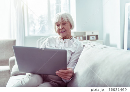 Beaming dark-eyed elderly lady having video chat with daughter using laptop 56021469