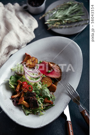 beef tagliata with vegetables. Close-up, low key, gray background. 56043554