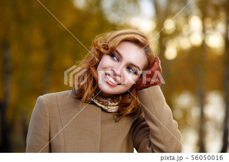 Stylish woman in beige coat and gloves standing in autumn yellow park. 56050016