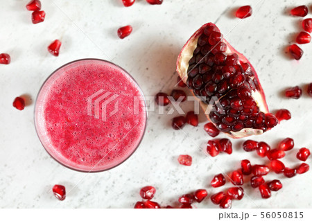 Glass with pink pomegranate smoothie, more berries and piece of fruit on white stone board next to Glass with pink pomegranate smoothie, more berries and piece of fruit on white stone board next to 56050815