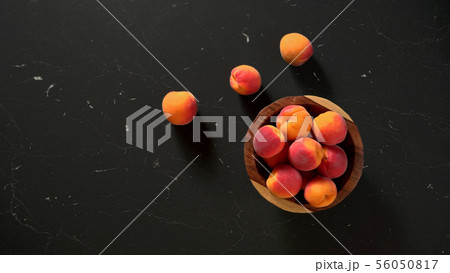 Flat lay photo - apricots in small wooden bowl, on black marble like table, space for text left side 56050817