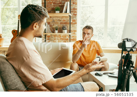 Two young male bloggers with professional camera recording video interview at home Two young male bloggers with professional camera recording video interview at home 56051535