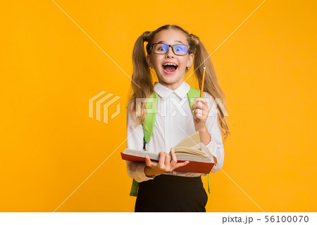 Excited Elementary Schoolgirl Holding Book And Pencil On Yellow Background 56100070