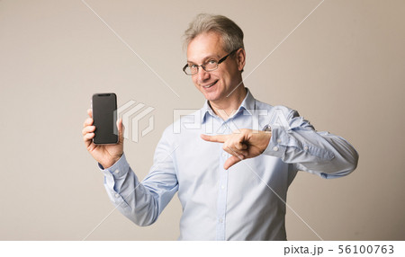 Senior man presenting smartphone and pointing on it Senior man presenting smartphone and pointing on it 56100763