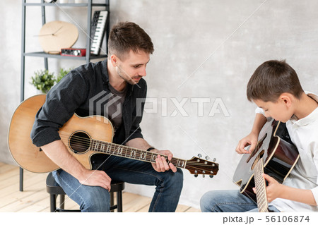 Young father watches his son learn to play guitar. Family music education Young father watches his son learn to play guitar. Family music education 56106874
