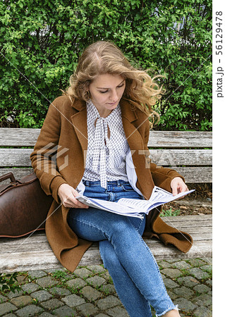 Woman sitting on bench and holding notes in hand Woman sitting on bench and holding notes in hand 56129478