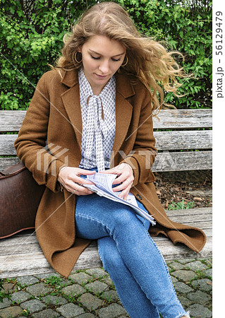 Woman sitting on bench and holding notes in hand Woman sitting on bench and holding notes in hand 56129479