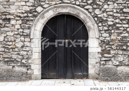 Closed black wooden door in stone wall 56144317
