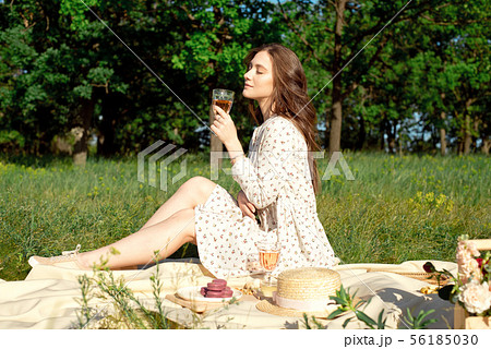 Cropped shot of a girl, in a summer dress, sitting with a glass of wine at a picnic while enjoying a 56185030