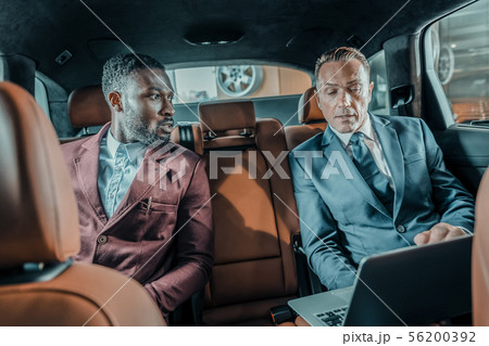 Two men sitting on the backseat of the car. 56200392