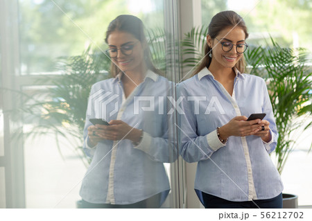 Delighted young office worker looking at her gadget Delighted young office worker looking at her gadget 56212702