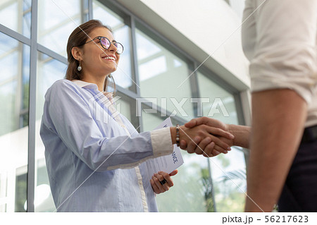 Delighted office worker shaking hands with her partner Delighted office worker shaking hands with her partner 56217623