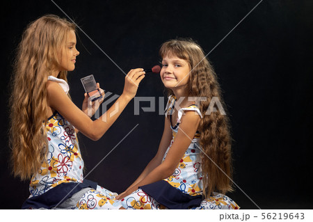 The older sister is applying powder to the younger The older sister is applying powder to the younger 56219643