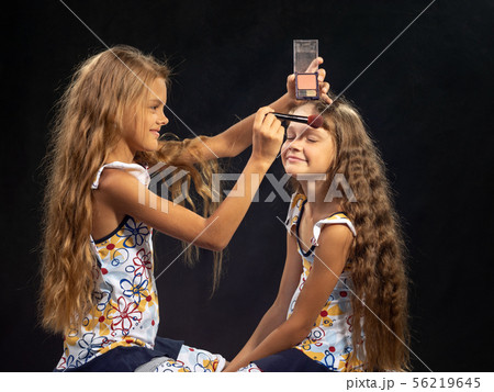 Girl puts powder on the forehead of another girl Girl puts powder on the forehead of another girl 56219645