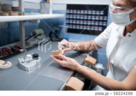 Dental technician polishing denture during her working day. Dental technician polishing denture during her working day. 56224209
