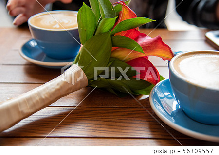 Cappuccino on a blue mug by a flower bouquet Cappuccino on a blue mug by a flower bouquet 56309557