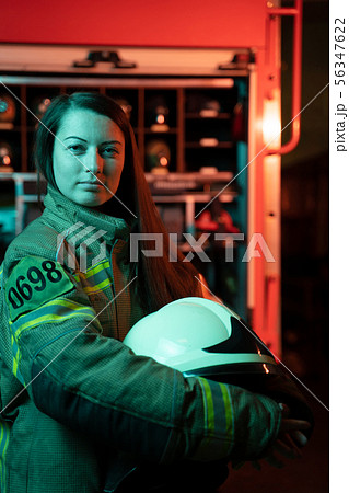 Photo of girl firefighter with long hair with helmet in her hands at fire station. Photo of girl firefighter with long hair with helmet in her hands at fire station. 56347622