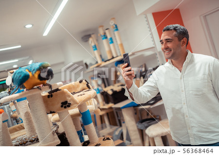 Grey-haired man smiling while taking picture of parrot 56368464