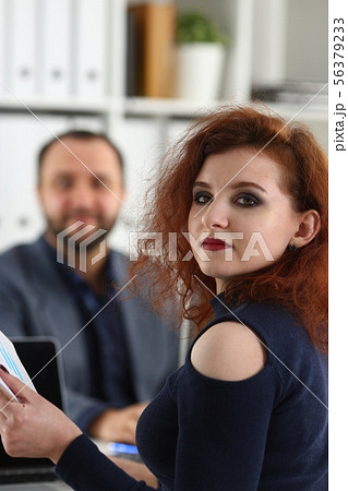 young beautiful red haired woman sit on chair at table in office in cabinet of her boss hold binder 56379233