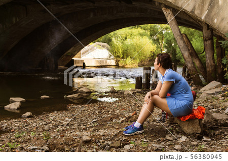 woman smokes while sitting alone under a bridge 56380945