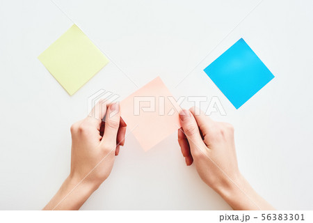 Hands holding an orange notepaper or postit isolated on white background Hands holding an orange notepaper or postit isolated on white background 56383301