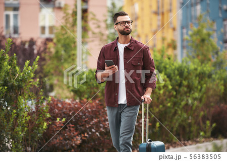 Where i am Handsome bearded man in casual wear and eyeglasses pulling his luggage and holding Where i am Handsome bearded man in casual wear and eyeglasses pulling his luggage and holding 56383505