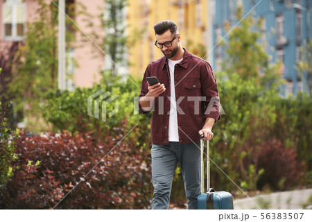 Chatting with friend. Handsome bearded man in casual wear and eyeglasses pulling his luggage and Chatting with friend. Handsome bearded man in casual wear and eyeglasses pulling his luggage and 56383507
