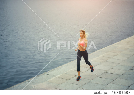Just running. Full length of young and active blonde woman in sports clothing running along the Just running. Full length of young and active blonde woman in sports clothing running along the 56383603