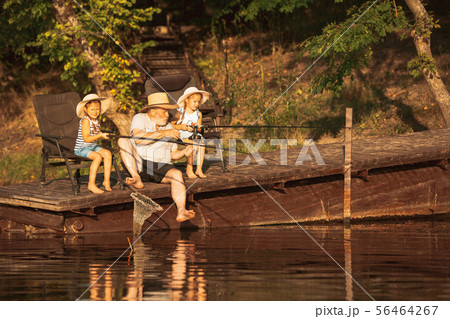 Cute little girls and their granddad are on fishing at the lake or river 56464267