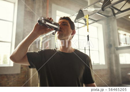 Refreshing. Young athletic man drinking fresh water from the bottle while exercising at gym Refreshing. Young athletic man drinking fresh water from the bottle while exercising at gym 56465205