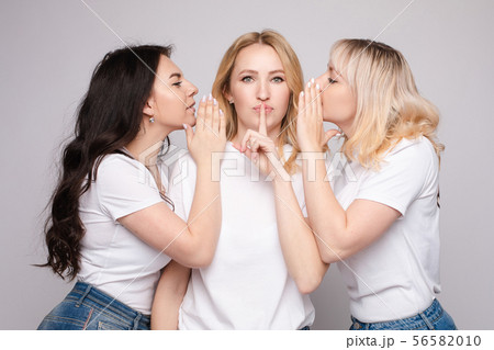 Gossiping girls whispering a secret to their Gossiping girls whispering a secret to their 56582010