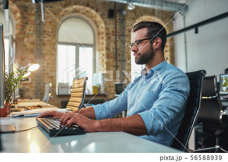 Successful businessman. Young bearded man in eyeglasses and formal wear working on computer while Successful businessman. Young bearded man in eyeglasses and formal wear working on computer while 56588939