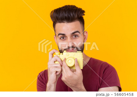 Portrait of a positive handsome young man with a beard holding a yellow vintage camera in his hands 56605458