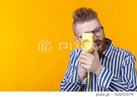 Unidentified young man with a yellow camera with a mustache and a beard on a yellow background 56605974