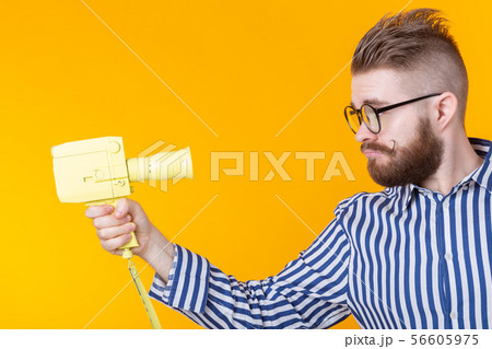 Unidentified young man with a yellow camera with a mustache and a beard on a yellow background 56605975