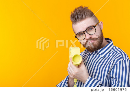 Unidentified young man with a yellow camera with a mustache and a beard on a yellow background 56605976