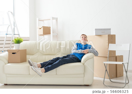 Relocation, new house and children concept - Satisfied happy teen boy lies on the sofa during moving 56606325