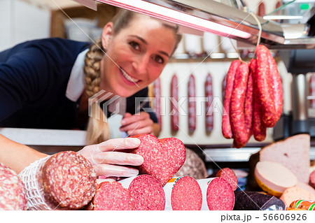 Sales woman in meat shop showing a heart shaped sausage Sales woman in meat shop showing a heart shaped sausage 56606926