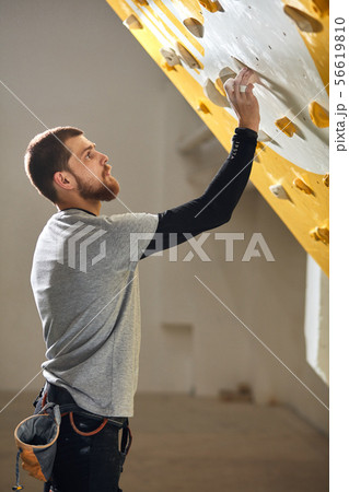 Young boulderer checking artificial rock wall before climbing training class 56619810