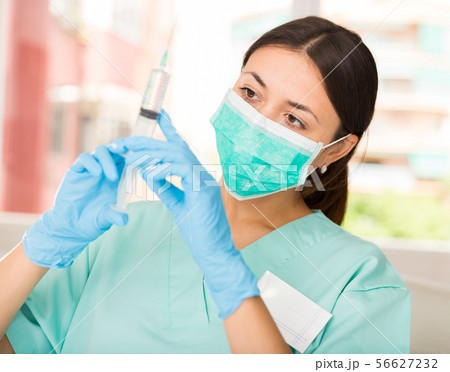 Girl nurse in mask holding syringe for injection in clinic Girl nurse in mask holding syringe for injection in clinic 56627232