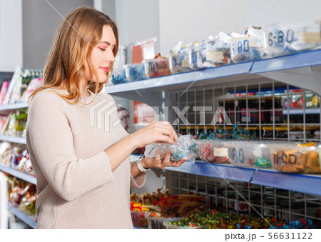 Positive woman buyer picking different candies in cellophane bag in store Positive woman buyer picking different candies in cellophane bag in store 56631122